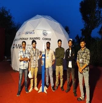 Five team members standing in front of an inflatable dome at the ISRO rocketry competition venue at night.